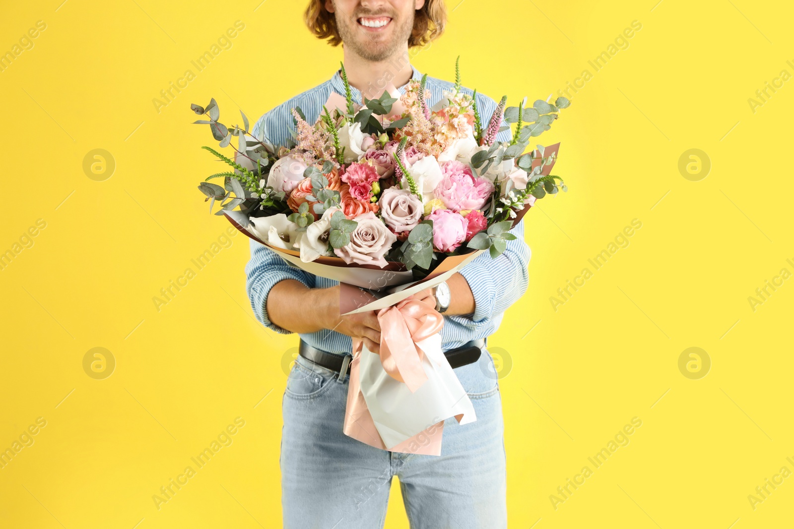 Photo of Man holding beautiful flower bouquet on yellow background, closeup view