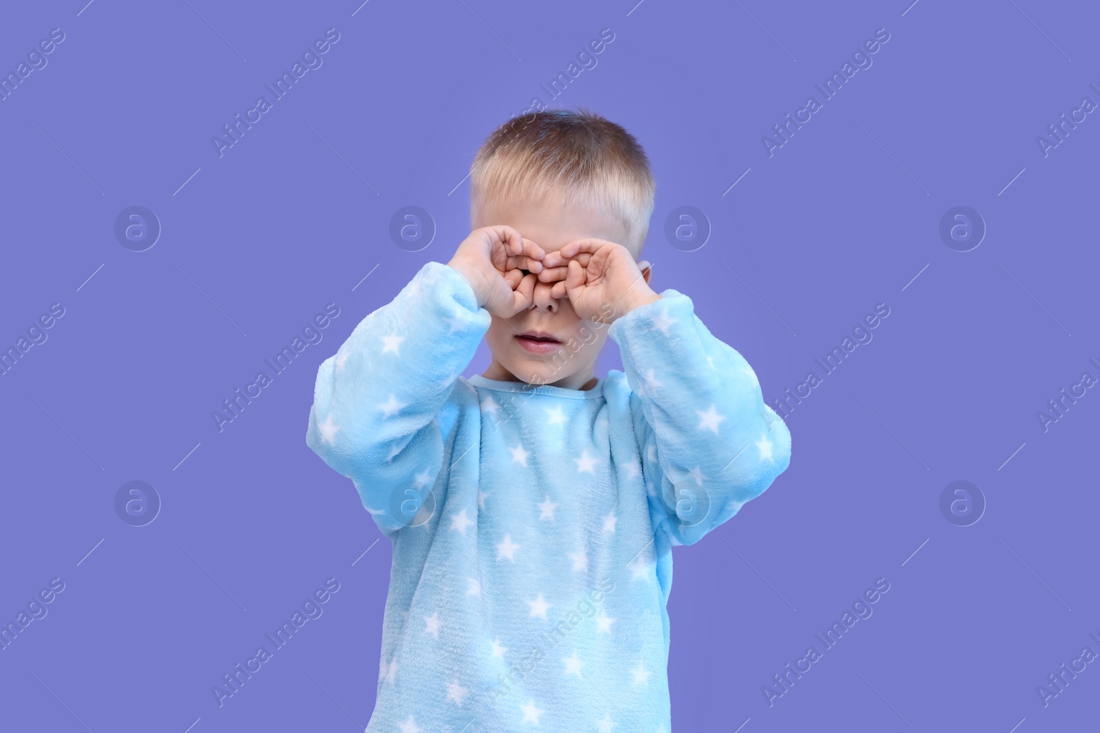 Photo of Sleepy boy rubbing his eyes on purple background. Insomnia problem
