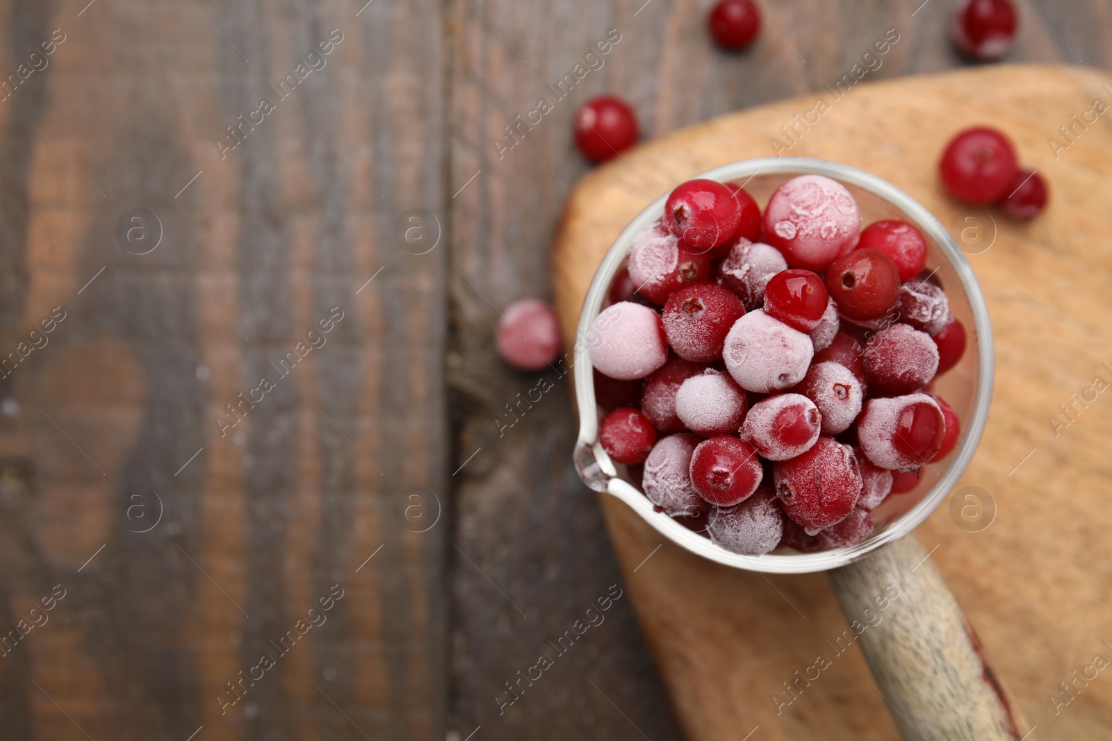 Photo of Frozen red cranberries in glass pot on wooden table, top view. Space for text