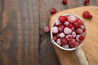 Frozen red cranberries in glass pot on wooden table, top view. Space for text