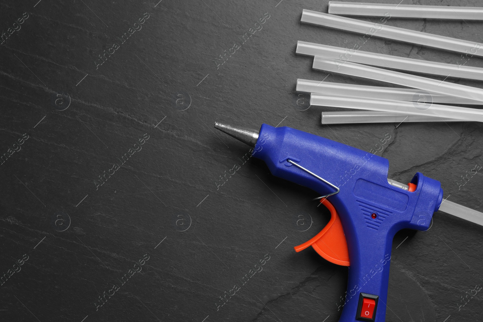 Photo of Blue glue gun and sticks on black table, flat lay. Space for text