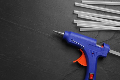 Photo of Blue glue gun and sticks on black table, flat lay. Space for text