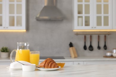 Breakfast served in kitchen. Fresh croissant, jam, honey and orange juice on white table. Space for text