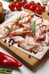 Slices of raw bacon and fresh products on white table