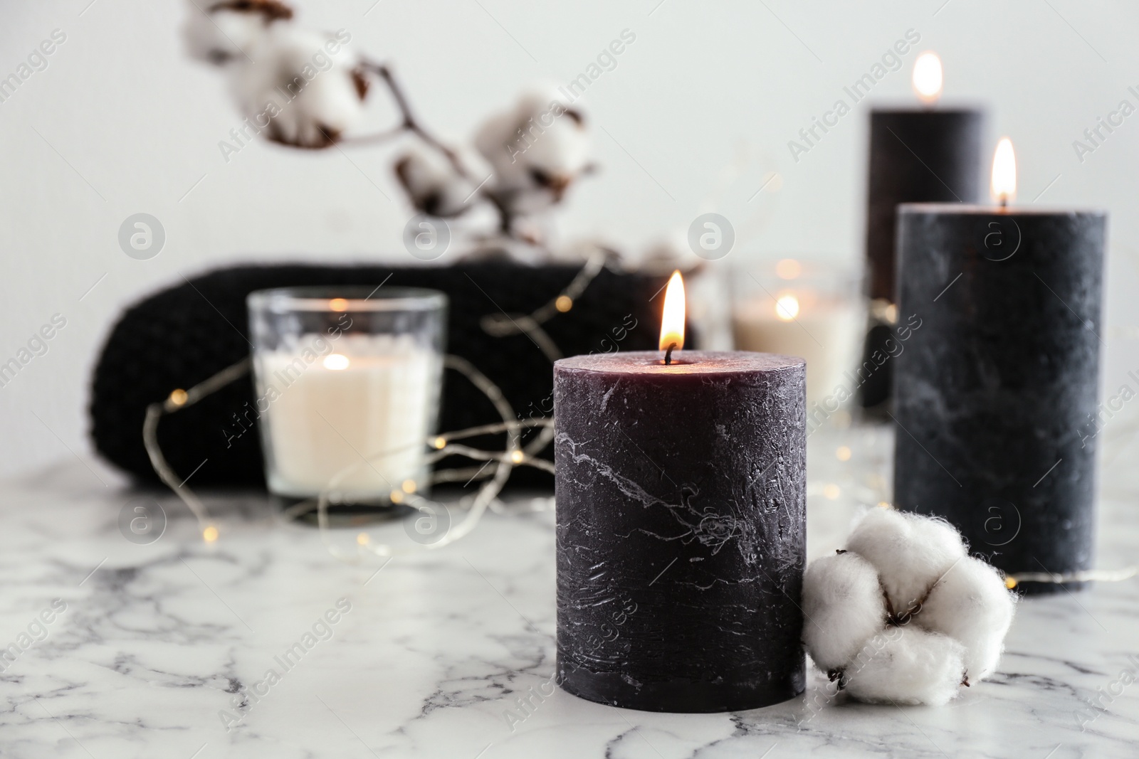 Photo of Burning candles and cotton flower with fairy lights on marble table