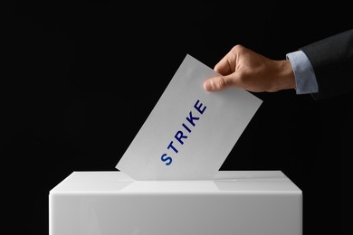 Man putting his vote with word Strike into ballot box on black background, closeup