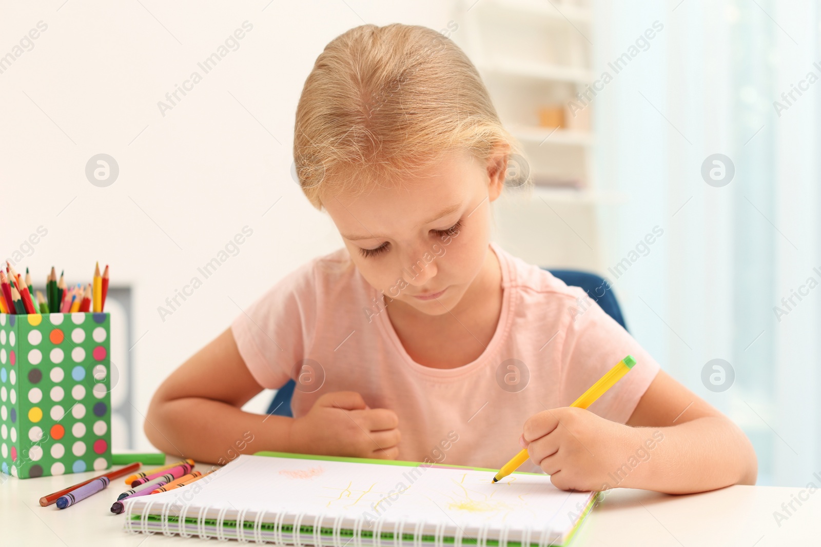 Photo of Cute little left-handed girl drawing at table in room