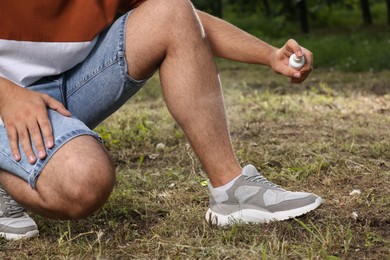 Photo of Man applying insect repellent on leg in park, closeup. Tick bites prevention
