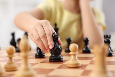 Photo of Little child playing chess indoors, closeup view