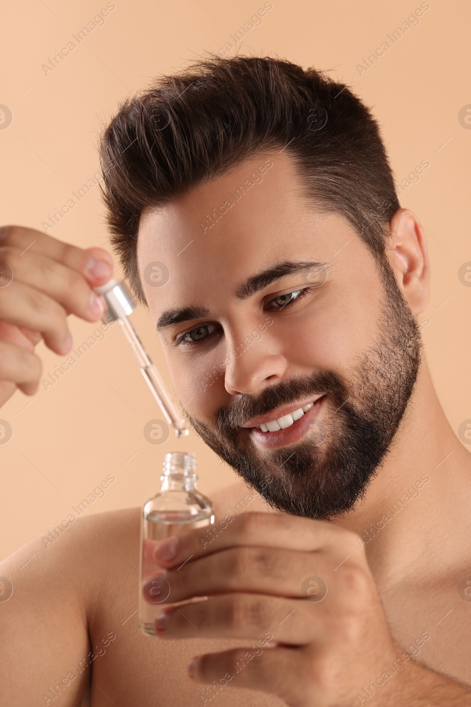 Photo of Handsome man with cosmetic serum in hands on beige background