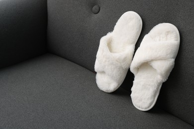 Photo of Soft white slippers on grey sofa, space for text