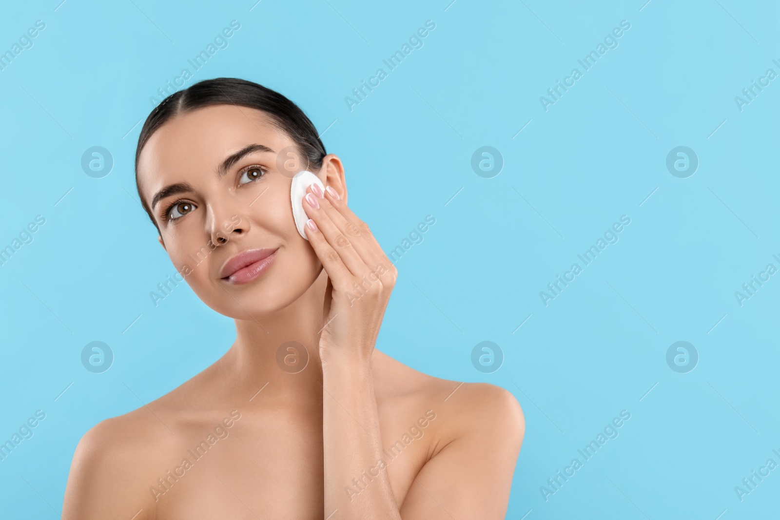 Photo of Beautiful woman removing makeup with cotton pad on light blue background, space for text