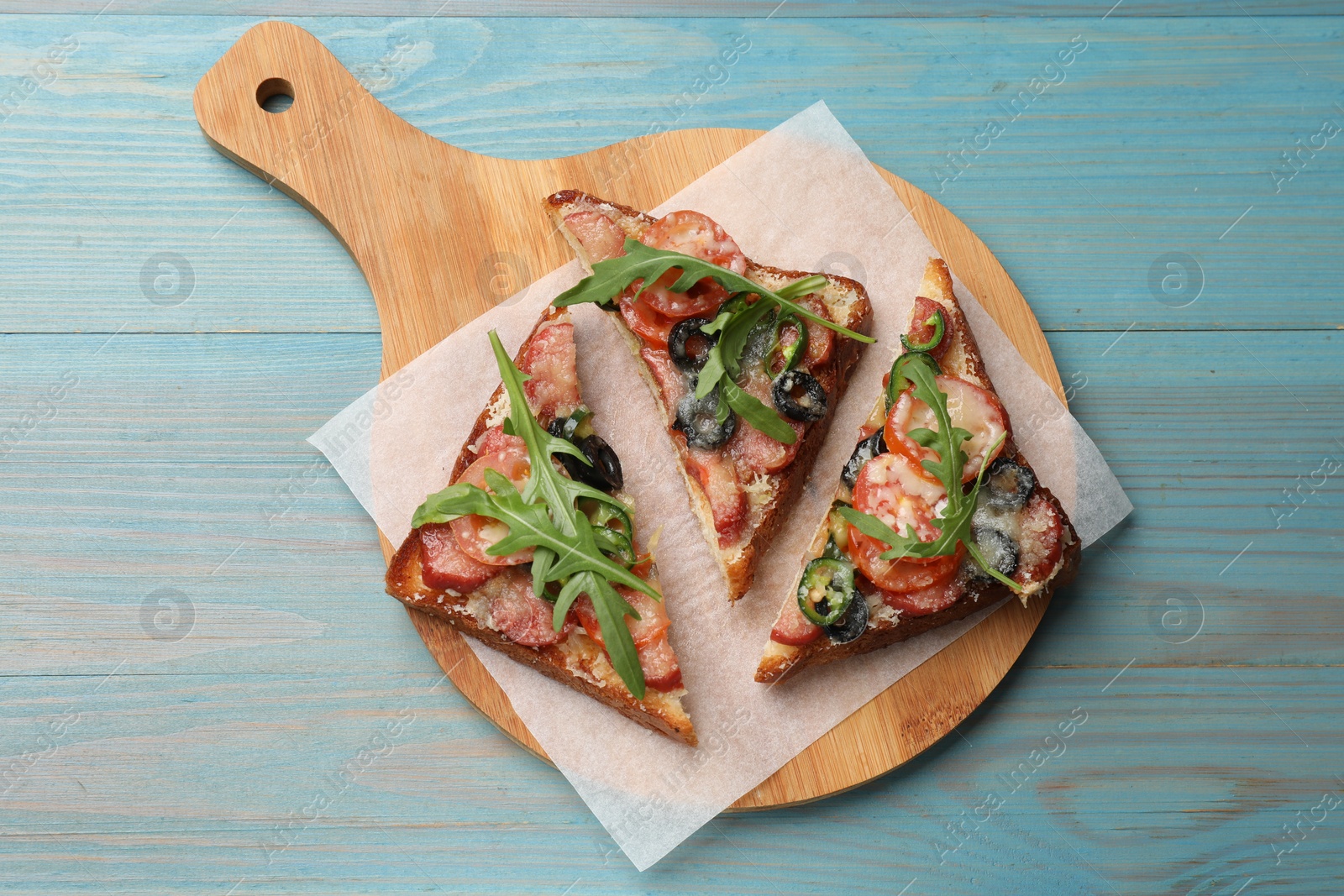 Photo of Tasty pizza toasts on light blue wooden table, top view