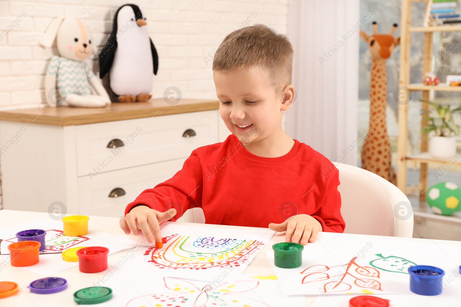 Photo of Little boy painting with finger at white table indoors