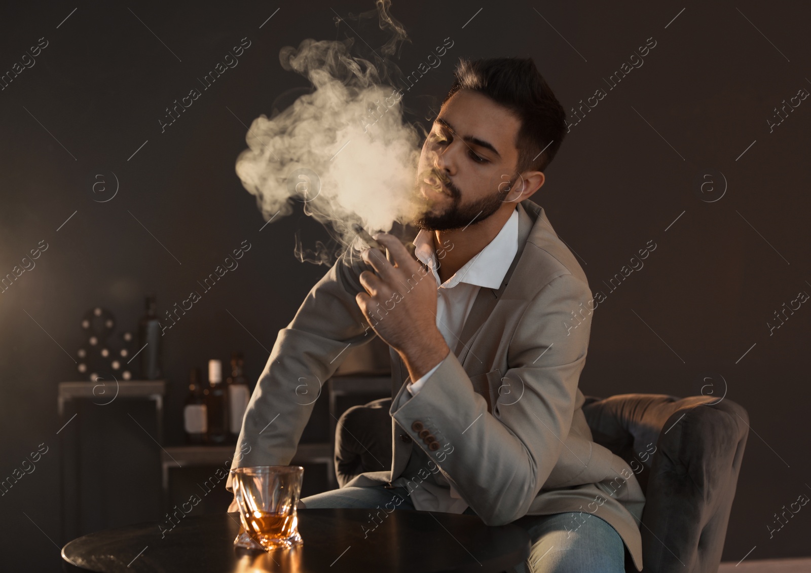 Photo of Man with glass of whiskey and cigar sitting at table indoors