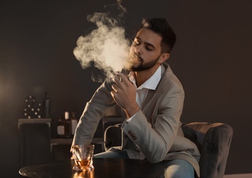 Man with glass of whiskey and cigar sitting at table indoors