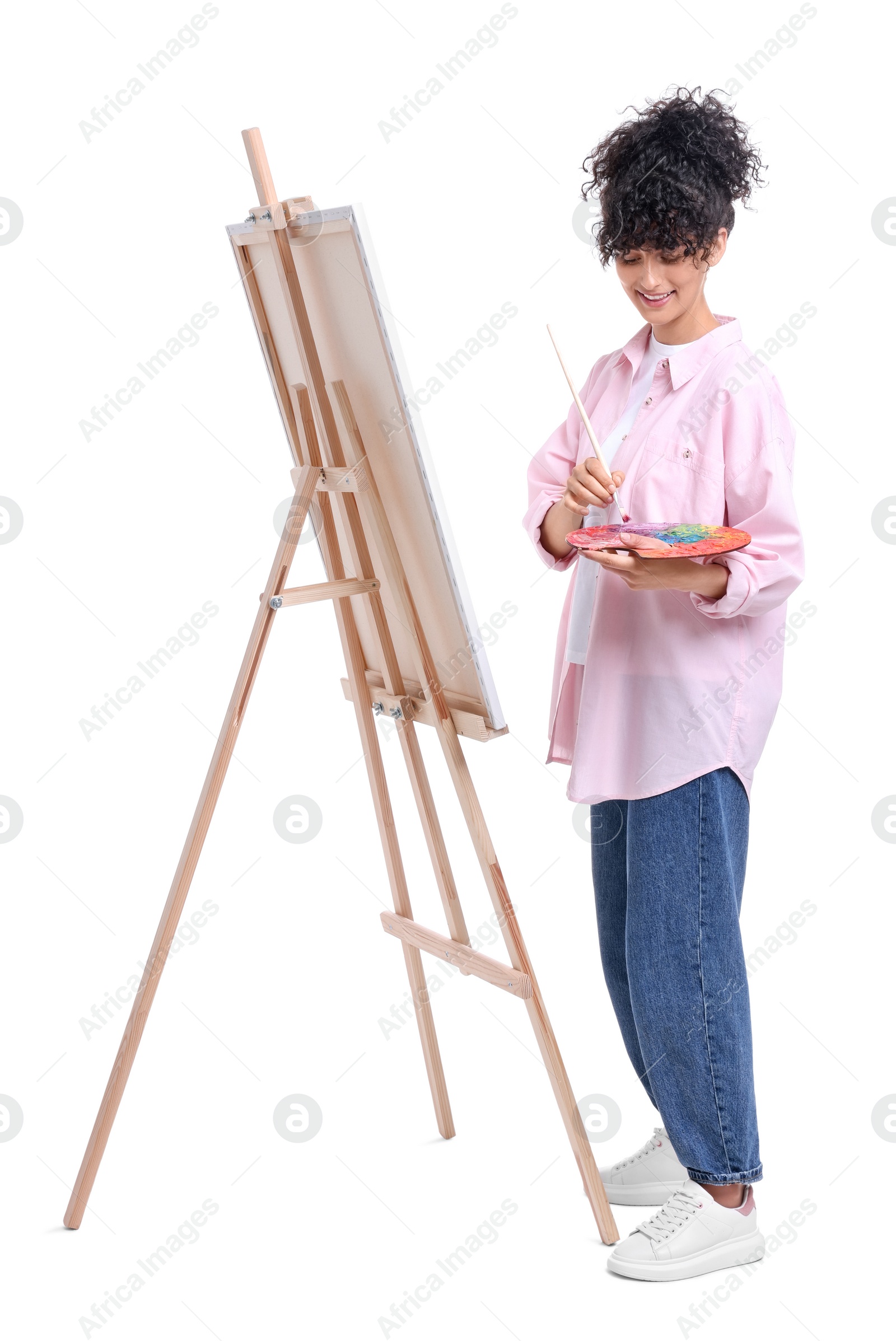 Photo of Young woman painting on easel with canvas against white background