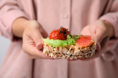 Photo of Woman holding crunchy buckwheat cakes with salmon, tomato and greens, closeup