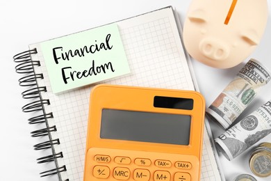 Notebook with words Financial Freedom, piggy bank, dollars and calculator on white table, flat lay