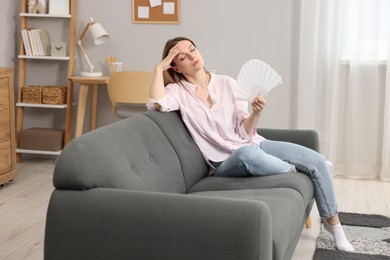 Woman waving white hand fan to cool herself on sofa at home