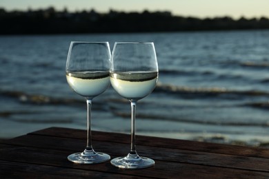 Photo of Two glasses of wine on wooden table near river at sunset. Space for text