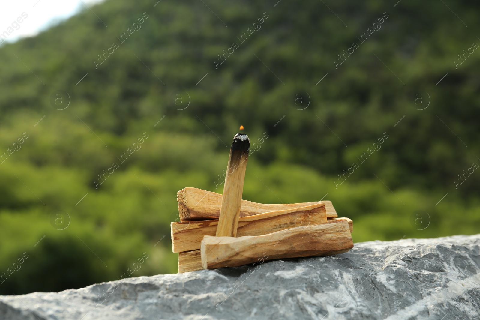 Photo of Burning palo santo stick on stone surface outdoors, closeup