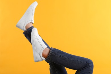 Photo of Man wearing stylish white sneakers on yellow background, closeup