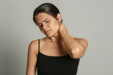 Young woman suffering from neck pain on grey background