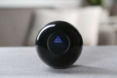 Photo of Magic eight ball with prediction Very Likely on light gray table, closeup