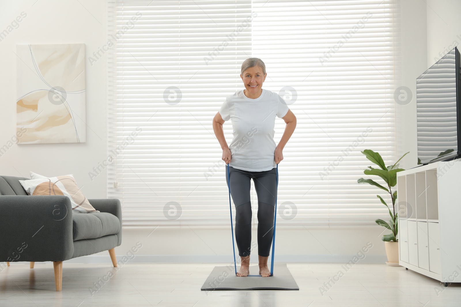 Photo of Senior woman doing exercise with fitness elastic band on mat at home