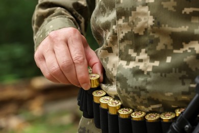 Man taking cartridges from belt outdoors, closeup. Hunting season