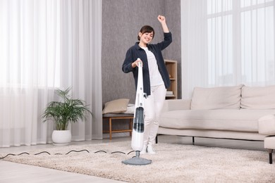 Happy young housewife vacuuming carpet at home