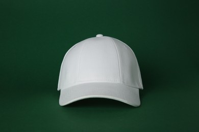 Photo of Stylish white baseball cap on dark green background