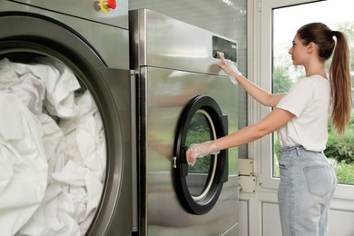 Young woman pressing buttons on washing machine in dry-cleaning