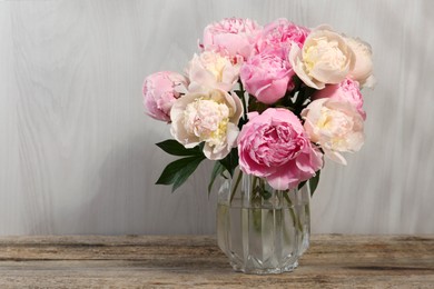 Beautiful peonies in vase on wooden table, space for text