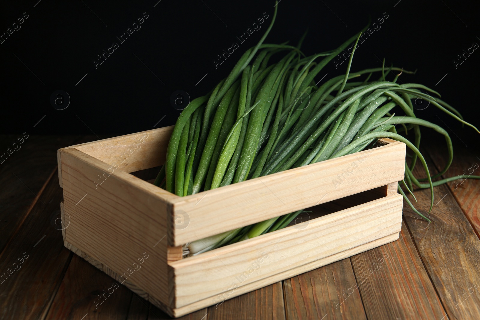 Photo of Fresh green spring onions in crate on wooden table