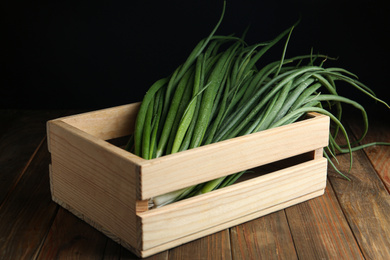 Photo of Fresh green spring onions in crate on wooden table