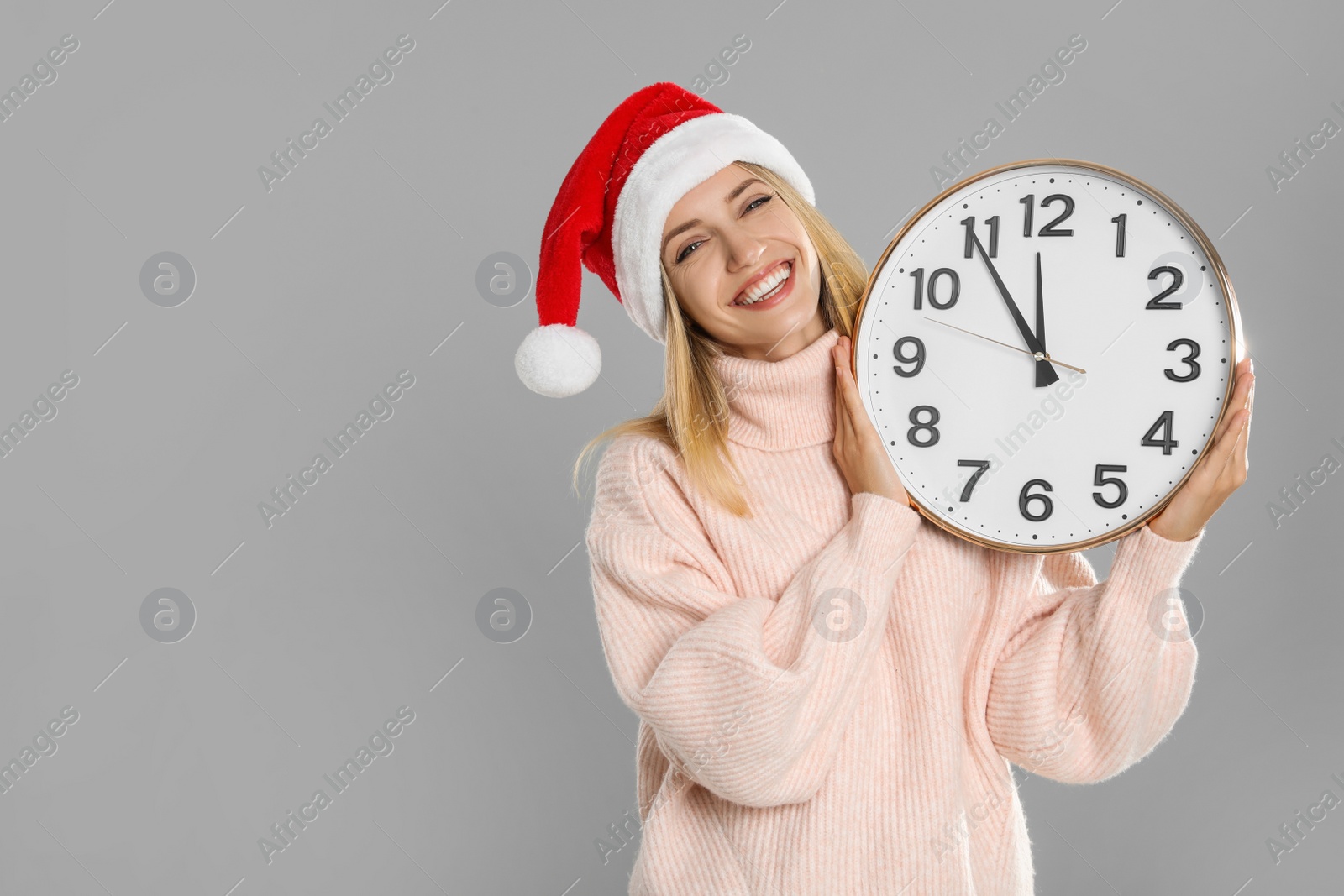 Photo of Woman in Santa hat with clock on grey background, space for text. New Year countdown
