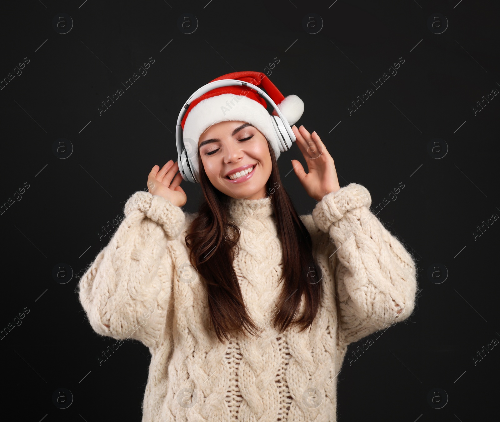 Photo of Young woman in Santa hat listening to Christmas music on black background