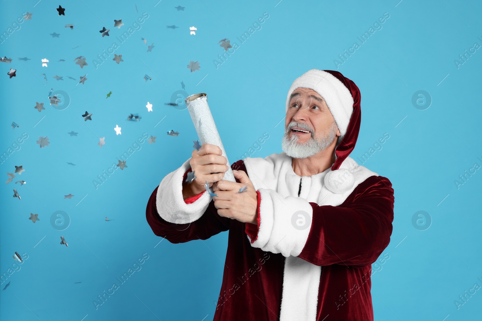 Photo of Man in Santa Claus costume blowing up party popper on light blue background