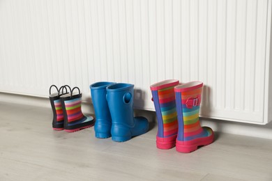 Different pairs of boots near modern radiator indoors