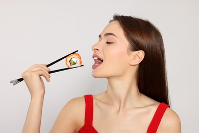 Photo of Beautiful young woman eating sushi roll with chopsticks on light background
