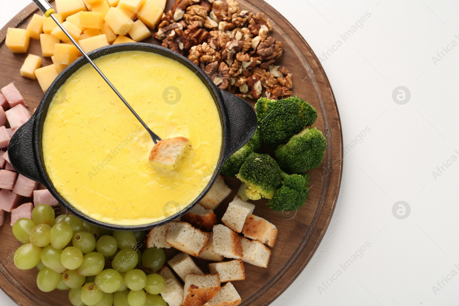 Photo of Fondue with tasty melted cheese, fork and different products on white table, top view