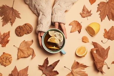 Photo of Woman in autumn sweater holding cup of hot cozy drink on color background, top view