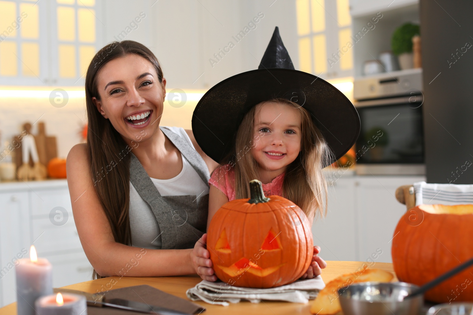 Photo of Mother and daughter with pumpkin jack o'lantern at table in kitchen. Halloween celebration