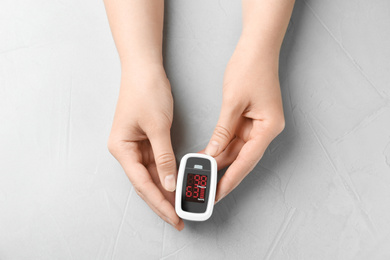 Photo of Woman holding fingertip pulse oximeter on light grey stone background, top view