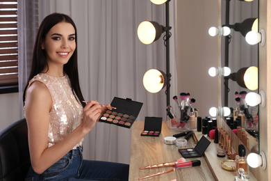 Beautiful young woman applying makeup near mirror in dressing room