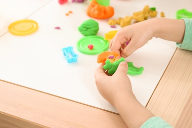 Cute little child using play dough at table, closeup