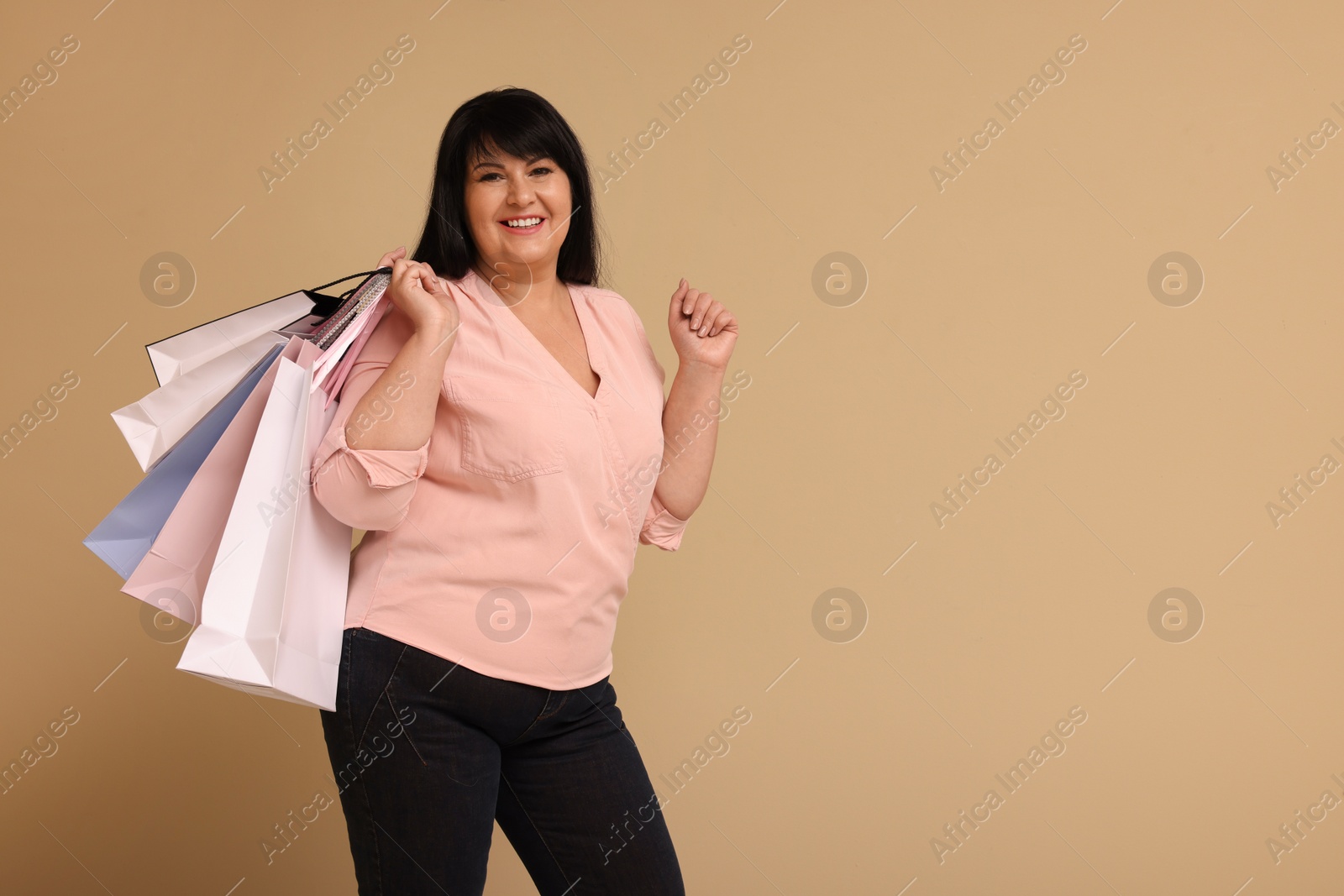 Photo of Beautiful overweight mature woman with shopping bags on beige background. Space for text