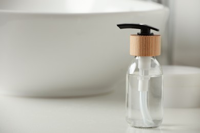 Bottle with dispenser cap on white table in bathroom, closeup. Space for text